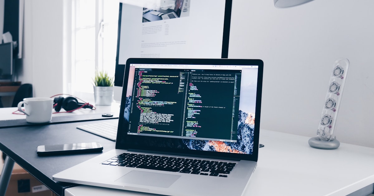 Modern webfejlesztési munkakörnyezet — MacBook laptop kóddal, fejlesztői asztalon